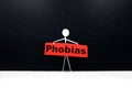 Human stick figure holding red Phobias word banner. Black background.