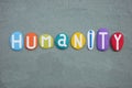 Humanity, social slogan composed with multi colored stone letters over green sand