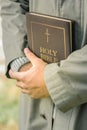 Humble man in light grey coat tightly holding hardcover bible Royalty Free Stock Photo