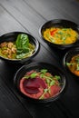 Hummus garnished peppers, chili, beet and herbs in black bowl on dark wooden table. Hummus assortment Royalty Free Stock Photo