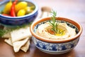 hummus in a terracotta bowl with rosemary sprig and pepper dippers