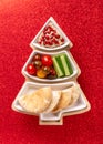 Hummus with vegetables and pita served on Christmas tree plate on shiny red background. Festive holiday snack. Top view