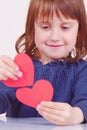 Humorous photo of cute little child girl playing with red hearts as symbol of amorousness