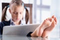 Humorous portrait of business child girl with bare feet on the table is working in office after lockdown. Selective focus