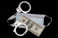 A hundred dollar bill and handcuffs lie on a protective medical mask on a black background. Royalty Free Stock Photo