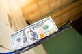 A hundred dollar bill hangs on an electrical cable attached to a bare aerated concrete brick wall close-up against a blurred