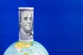 A hundred-dollar bill on top of the globe on a blue background Royalty Free Stock Photo