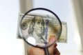 Hundred dollar bill under magnifying glass is being inspected Conceptual photo on window background