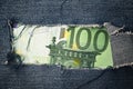Hundred euros bill through torn blue jeans texture
