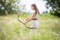 A Hungarian woman in a linen dress standing with a bow in the tall grass Royalty Free Stock Photo