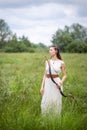 A Hungarian woman in a linen dress standing with a bow in the tall grass Royalty Free Stock Photo