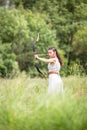 A Hungarian woman in a linen dress standing with a bow in the tall grass Royalty Free Stock Photo