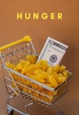 HUNGER text against Shopping trolley cart Filled With Pasta with 5 US dollar paper money banknote on Beige background