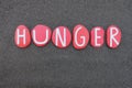 Hunger word composed with red colored stone letters over black volcanic sand