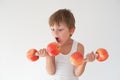 Hungry active strong small child in tank top lifting dumbbells made from apples fruits wishing to bite and eat food