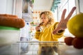 Hungry beautiful adult young woman eat sweet cake croissant and open the fridge to look for other food - diet and food concept - Royalty Free Stock Photo