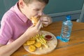 Hungry boy eagerly bites a burger during lunch in a fast food cafe