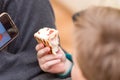 A Hungry boy eating a hot dog at home sit while playing with the smartphone.Close-up