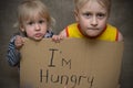 A hungry boy and a girl with a cardboard tablet with the inscription I`m hungry . The social problem.