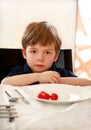 Hungry child sitting in chair at table in kitchen and waiting for meal and lunch. Boy is curious what he will get for meal. Royalty Free Stock Photo