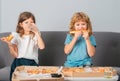 Hungry children eating pizza. Two young children bite pizza indoors.