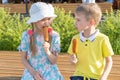 Hungry children eating street food sitting on a park bench. A boy and a girl eating fried sausages on a stick