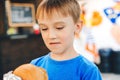 Hungry cute boy holds a burger at outdoors cafe. Happy child eating fast food. Childhood, unhealthy food concept Royalty Free Stock Photo