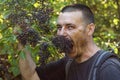 Hungry dark-haired tourist eagerly bites an elderberry on a tree against a background of green foliage