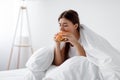 Hungry after diet, starving stressed caucasian millennial woman eating burger in bed Royalty Free Stock Photo