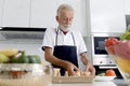 Hungry elderly man wearing apron at kitchen counter with colorful fresh vegetables and fruits. Senior man holding bread for