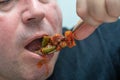 A hungry and fat fat man eagerly eats roasted meat with spices, fat from his mouth flows through his beard