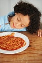 Hungry, food and child eating spaghetti by the wooden kitchen counter for lunch at home. Pasta, tomato and boy kid