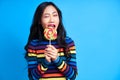 Hungry funny woman bite delicious colorful lollipop isolated on blue background