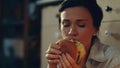 Hungry girl eating burger on floor. Young woman drinking red wine at home.