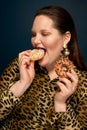 A hungry girl in a leopard blouse eats a donut appetizingly. Dark blue background.