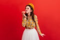 Hungry girl in stylish outfit bites strawberry donut. Portrait of woman in checkered blouse and orange beret on bright Royalty Free Stock Photo