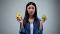 Hungry girl trying to choose between donut and apple, healthy eating, temptation Royalty Free Stock Photo