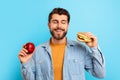 Hungry Guy Holding Burger And Apple Choosing Over Blue Background Royalty Free Stock Photo