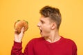 Hungry guy holds an appetizing burger in his hands and reacts emotionally. Close up Portrait of a surprised man with a burger in Royalty Free Stock Photo
