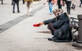 Hungry homeless beggar woman beg for money on the urban street in the city from people walking by, social documentary concept