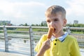 Hungry kid eating street food on the beach in summer. A little emotional boy eating fried sausages on a stick