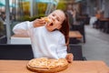 Hungry kid girl in white sweatshirt eating pizza with appetite on cafe terrace. outdoors restaurant copy space Royalty Free Stock Photo