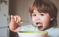 Hungry little boy eating. Cheerful baby child eats food itself with spoon. Tasty kids breakfast. Baby eating food on Royalty Free Stock Photo