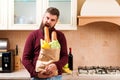 Hungry man bites baguette at kitchen. Bearded man holding paper bag with food at home. Delivery food, products to home