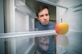 Hungry man is looking for food in fridge. Only apple is inside empty fridge Royalty Free Stock Photo