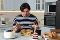 Hungry overweight man at table with sweets and fast food in kitchen