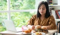 Hungry overweight woman holding hamburger on a wooden plate, Fried Chicken and Pizza on table, During work from home, gain weight