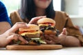 Hungry overweight woman holding hamburger on a wooden plate, During work from home, gain weight problem. Concept of binge eating