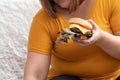 Hungry overweight woman smiling and holding hamburger and sitting in the bedroom, her very happy and enjoy to eat fast food. Conce