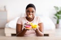 Hungry plus size black woman having weight loss diet, wearing adhesive bandages on mouth, holding plate with sweets Royalty Free Stock Photo